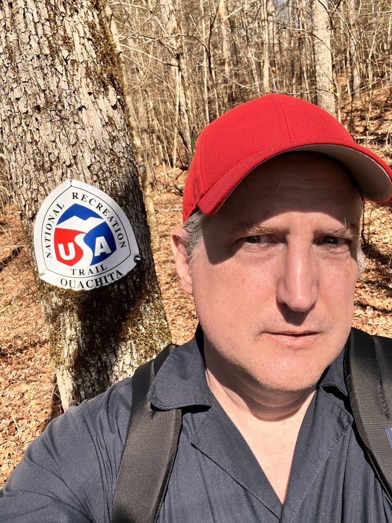 Person taking a selfie on the Ouachita National Recreation Trail with a sign visible behind them.